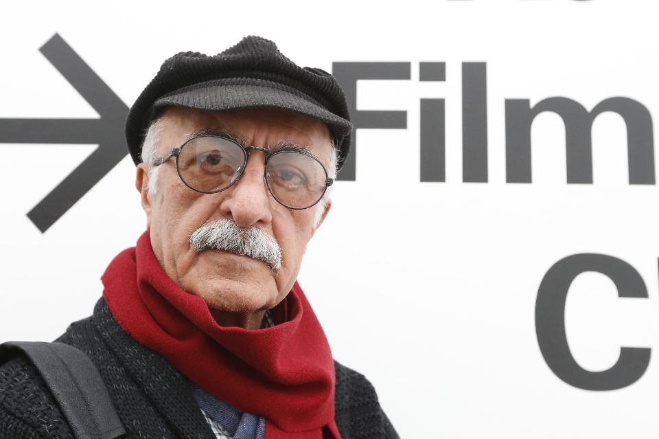 Iranian filmmaker Kamran Shirdel poses beside the sign pointing to where some of his films can be seen at the Carnegie Museum of Art Thursday, Feb. 20, 2014, during his first visit to the U.S. Shirdel began making gritty films of taboo subjects in the 1960s. (AP Photo/Keith Srakocic)