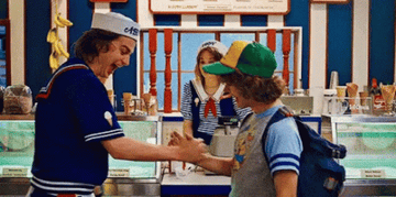 Steve Harrington and Dustin Henderson from "Stranger Things" shake hands and laugh in an ice cream parlor