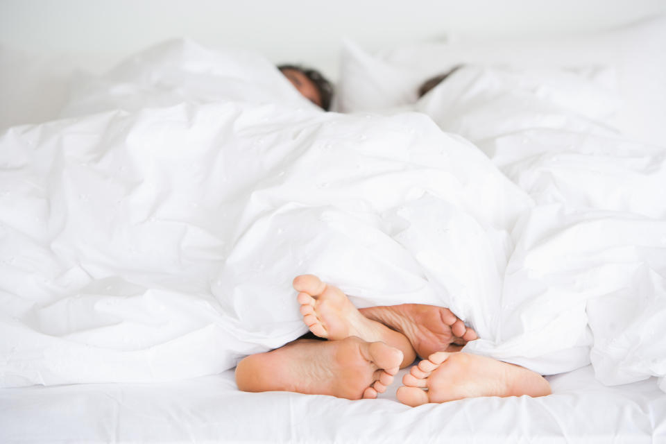 Two people's feet sticking out from under a white duvet, suggesting intimacy