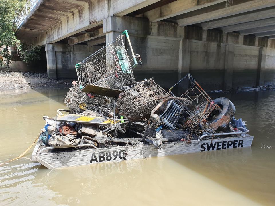 A boat filled with garbage including shopping trolleys floats in Cooks River, Sydney.