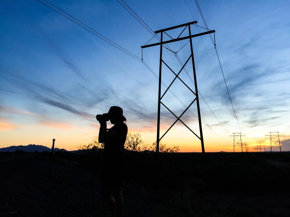 A silhouette of the author holding a camera with a sunset and cable towers in the background.