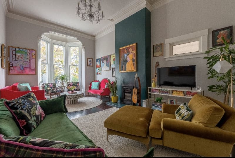 White living room with green velvet sofa and gold velvet armchair, bay window, and teal accent wall