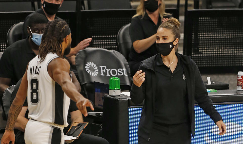 Becky Hammon, wearing a mask, talks to Patty Mills during a break in play. 