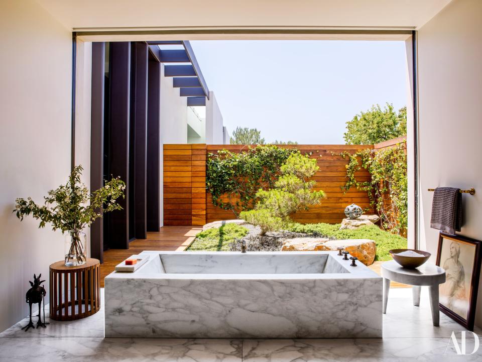 In the master bath, a custom Calacatta marble tub by Shadley with Waterworks fittings looks out on a courtyard garden. Vintage rosewood stool from JF Chen.