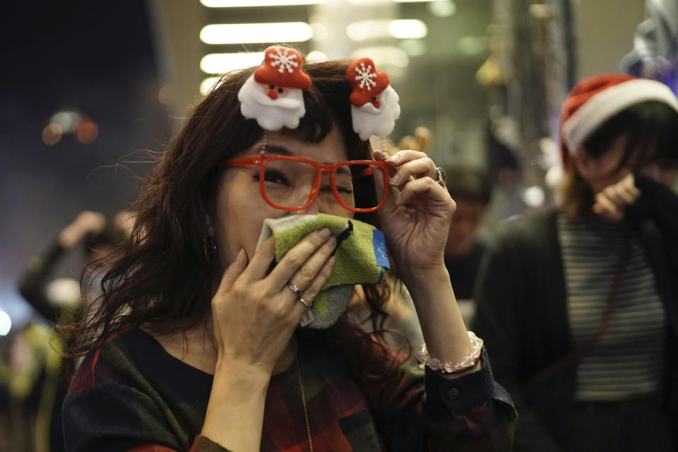 A woman wearing Christmas decorations in her hair reacts to tear gas as police confront protesters on Christmas Eve in Hong Kong on Tuesday, Dec. 24, 2019. More than six months of protests have beset the city with frequent confrontations between protesters and police. (AP Photo/Kin Cheung)