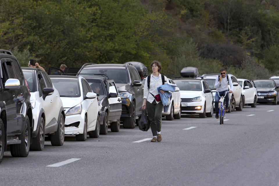 A young man walks as another rides his bicycle toward the border crossing between Georgia and Russia at Verkhny Lars, as they leave Chmi, North Ossetia–Alania Republic, Russia, Wednesday, Sept. 28, 2022. Long lines of vehicles have formed at a border crossing between Russia's North Ossetia region and Georgia after Moscow announced a partial military mobilization. (AP Photo)