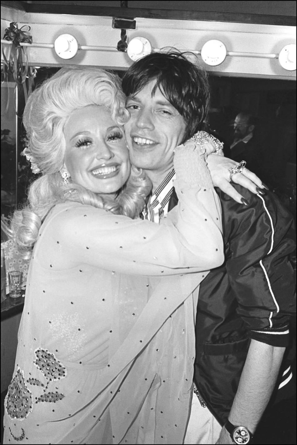 After her performance at the Bottom Line, American Country musician Dolly Parton hugs British rocker Mick Jagger backstage, New York, New York, May 14, 1977.