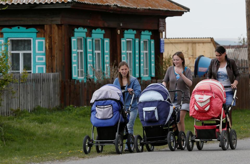 Women push carts with their babies along a street in the village of Malaya Inya in Siberia, Russia, in 2016. 