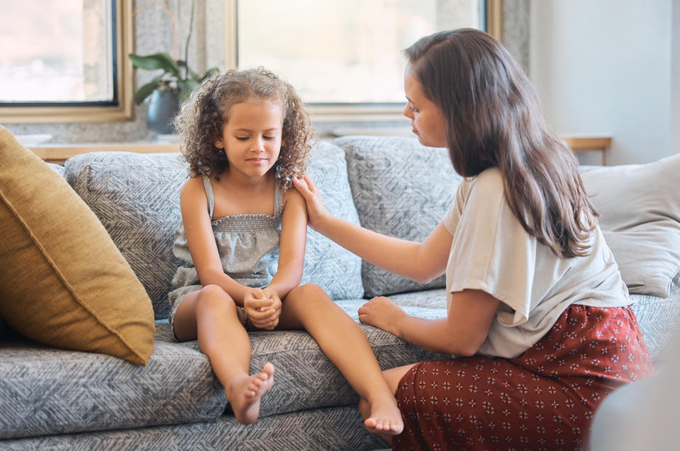 A woman comforts a sad little girl sitting on a couch