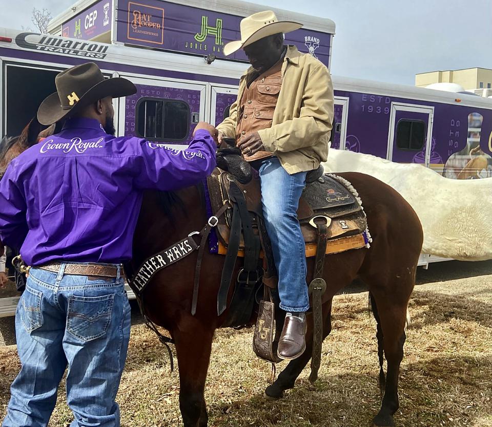 Tory Johnson, a Professional Rodeo Cowboys Association (PRCA) steer wrestler, helps William Calvin prepare for a ride on a horse on the back lawn of Fifth Street Baptist Church during the church's 2023 "Pioneer Day."