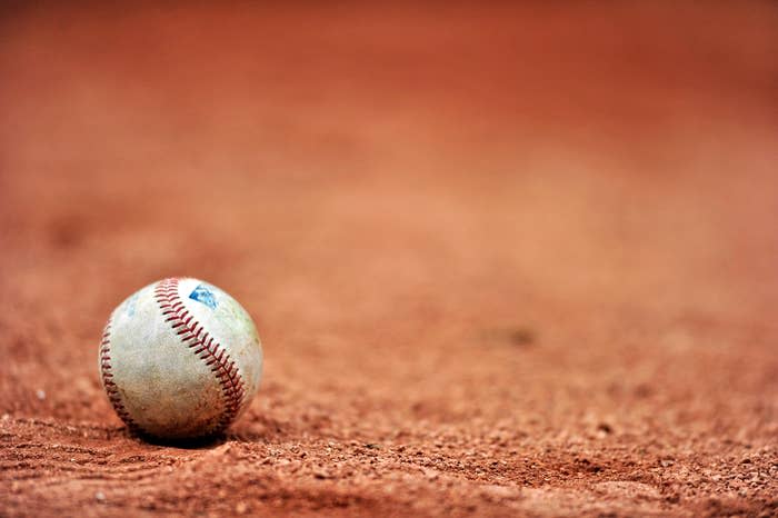 A close-up of a baseball resting on a clay baseball field