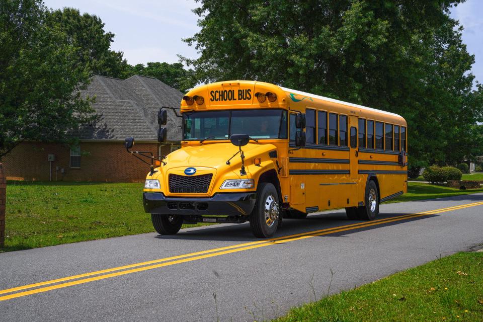 A yellow electric school bus drives down the road.