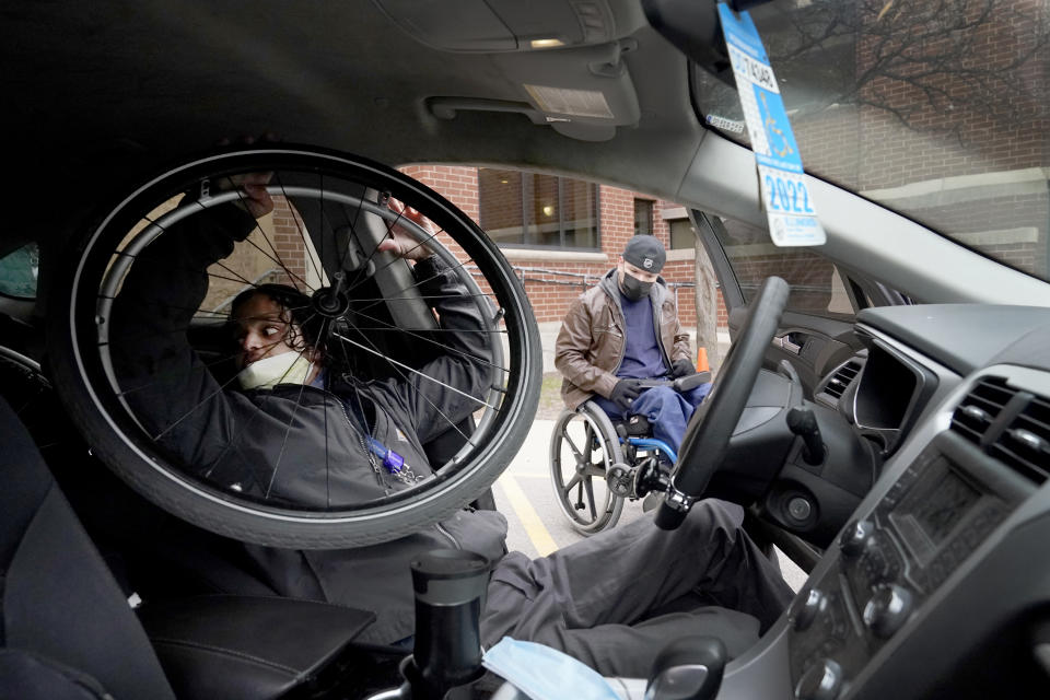 Jonathan Annicks, left, a part-time peer mentor for patients with spinal cord injuries at Schwab Rehabilitation Hospital, demonstrates to Cesar Romero how to get in and out of a car and dismantle a wheel chair for driving Tuesday, March 29, 2022, in Chicago. "If he can do it, I can do it," said Romero, a 45-year-old Chicagoan who worked construction until he was shot and paralyzed last year while on his way to a grocery store. (AP Photo/Charles Rex Arbogast)