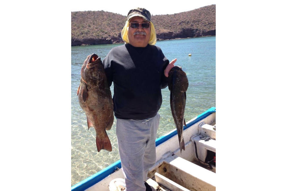 This undated photo provided by Azalia Sandoval, taken in Guaymas Bay, Mexico, shows Carlos Manuel Sandoval showing off the two fish he caught that day. Sandoval was born in Guaymas on Feb. 13, 1955, and he continued to hear the siren call of the sea more than a quarter-century after he and his family moved to Phoenix. He still traveled back to his hometown port and other coastal communities on Mexico's Sea of Cortez at least annually to indulge his passion for fishing. Sandoval died June 30 from complications of COVID-19 at age 65. (Courtesy of Azalia Sandoval via AP)