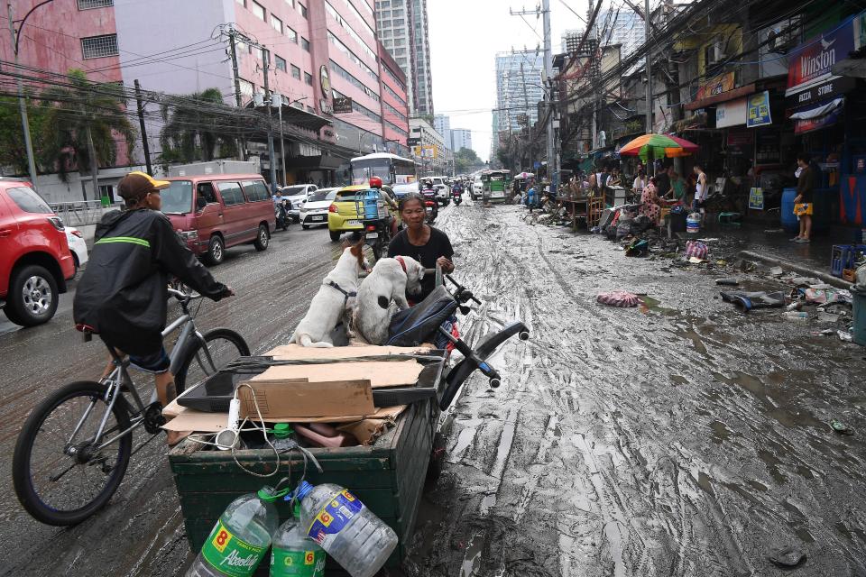 A resident pushes her cart loaded with her belongings and pet dogs along a mudded road in Manila (AFP via Getty Images)