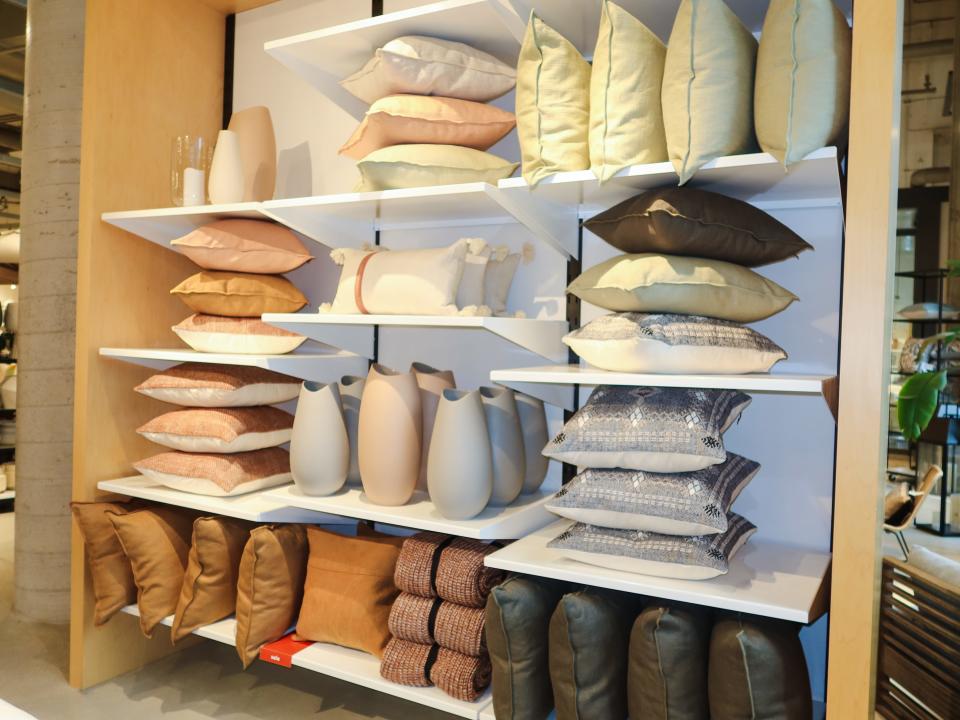 Several pillows on white shelves at West Elm. The pillows are tan, green, beige, and coral.