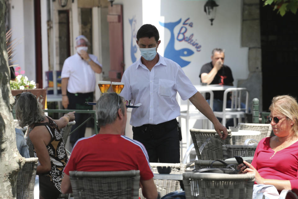 A bartender brings drinks to customers in a cafe of Saint Jean de Luz, southwestern France, Tuesday June 2, 2020. The French way of life resumes Tuesday with most virus-related restrictions easing as the country prepares for the summer holiday season amid the pandemic. Restaurants and cafes reopen Tuesday with a notable exception for the Paris region, the country's worst-affected by the virus, where many facilities will have to wait until June 22 to reopen. (AP Photo/Bob Edme)