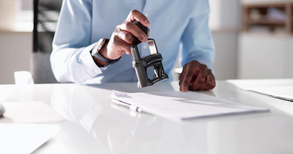 A person in professional attire stamps a document on a desk in an office setting