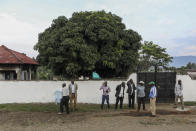 Plainclothes security forces and civilians stand outside the entrance to the Lhubiriha Secondary School following an attack on the school on Saturday, in Mpondwe, Uganda Sunday, June 18, 2023, near the border with Congo. Ugandan authorities have recovered the bodies of 41 people including 38 students who were burned, shot or hacked to death after suspected rebels attacked the school, according to the local mayor. (AP Photo/Hajarah Nalwadda)