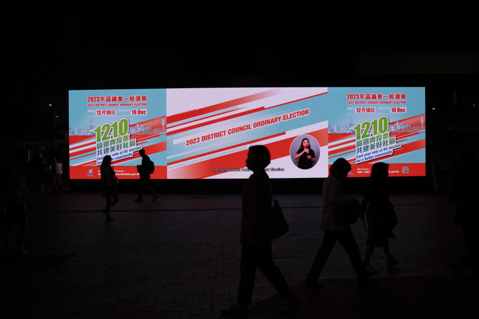 FILE - Pedestrians walk past an electronic billboard promoting the upcoming district council elections in Hong Kong, on Nov. 28, 2023. Residents went to the polls on Sunday, Dec. 10, in Hong Kong's first district council elections since an electoral overhaul was implemented under Beijing's guidance of “patriots” administering the city, effectively shutting out all pro-democracy candidates. (AP Photo/Louise Delmotte, File)