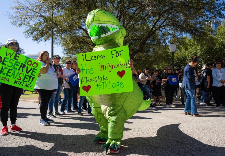 A protester wears a dinosaur costume Saturday while demanding driver's licenses for immigrants.