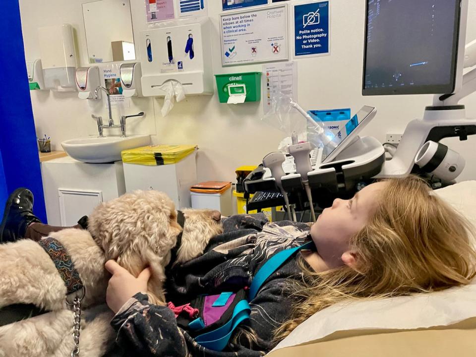 Sonia Hooykaas's daughter Eilidh Hooykaas lies on a hospital bed with her medical assistance dog.