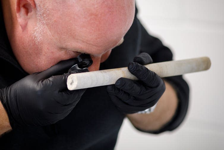 Man examining stone rod.