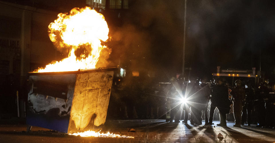 Tucson Police Department officers guard firefighters approaching a dumpster lit on fire by protestors rallying over the death of George Floyd, Sunday, May 31, 2020, in Tucson, Ariz. Protests were held throughout the country over the death of Floyd, a black man who died after being restrained by Minneapolis police officers on May 25. (Josh Galemore/Arizona Daily Star via AP)