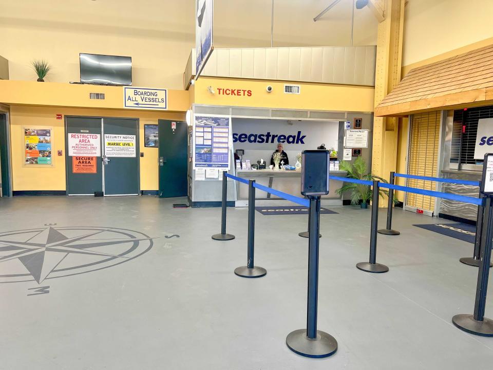 A room with gray floors, yellow walls, and a ticket booth with a worker staffed at the desk. Red lettering above the window says "tickets"