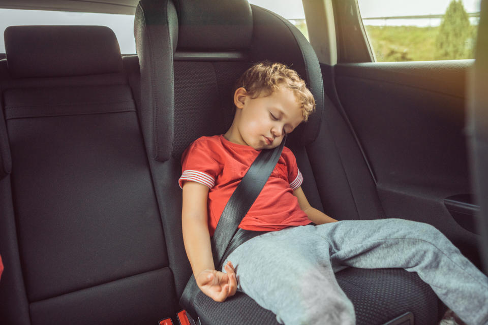 Child asleep in car booster seat as parents are warned about dangers of improper car restraints. 