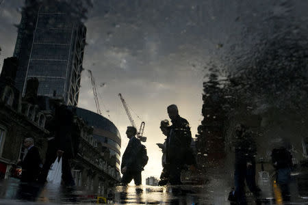 City workers are reflected in a puddle as they walk into the City of London, Britain October 16, 2017. Picture has been rotated 180 degrees. Picture taken October 16, 2017. REUTERS/Mary Turner