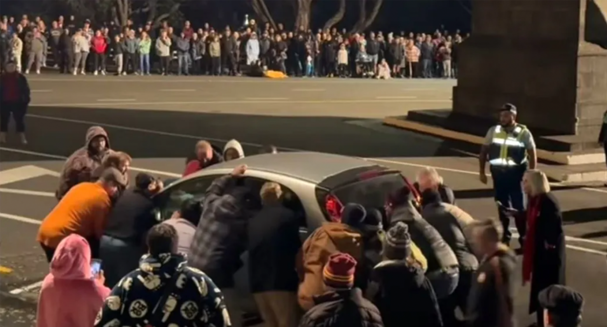 A group circle the car to pick it up and move it.