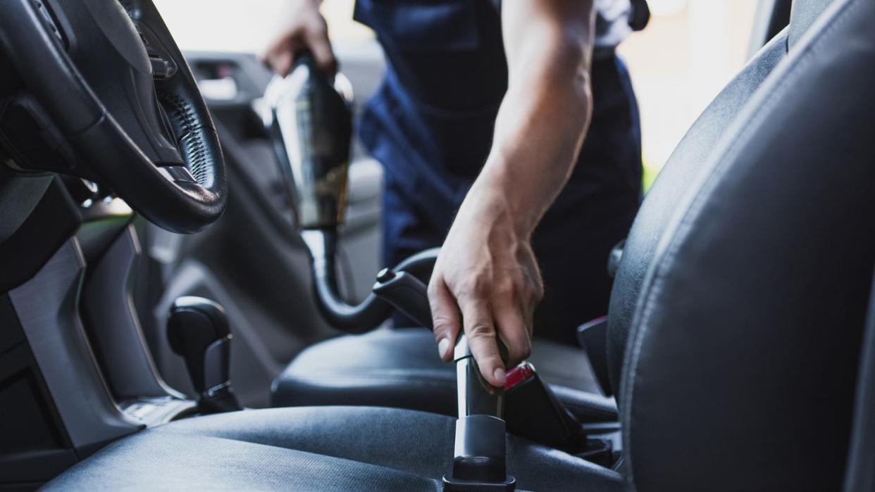 cropped view of car cleaner vacuuming drivers seat in car