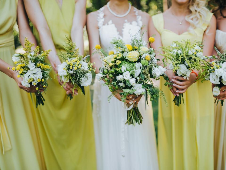 bride in a white dress and bridesmaids dresses are yellow and are holding bouquets of yellow flowers and greenery