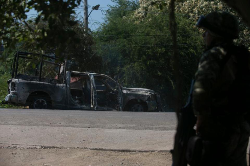 A soldier stands by a charred truck that belongs to Michoacan state police, after it was burned during an attack in El Aguaje, Mexico, on 14 October. At least 13 police officers were killed and three others injured Monday in the ambush.