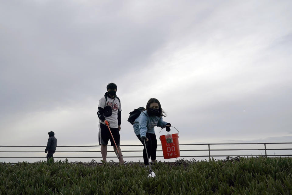 Pacifica Beach Coalition volunteers Alec Juntura, 21, foreground left, and Kimmy Tran, 20, pick up trash near Sharp Park Beach in Pacifica, Calif., Wednesday, March 17, 2021. Disposable masks, gloves and other personal protective equipment have safeguarded untold lives during the pandemic. They’re also creating a worldwide environmental problem, littering streets and sending an influx of harmful plastic into landfills and oceans. (AP Photo/Jeff Chiu)