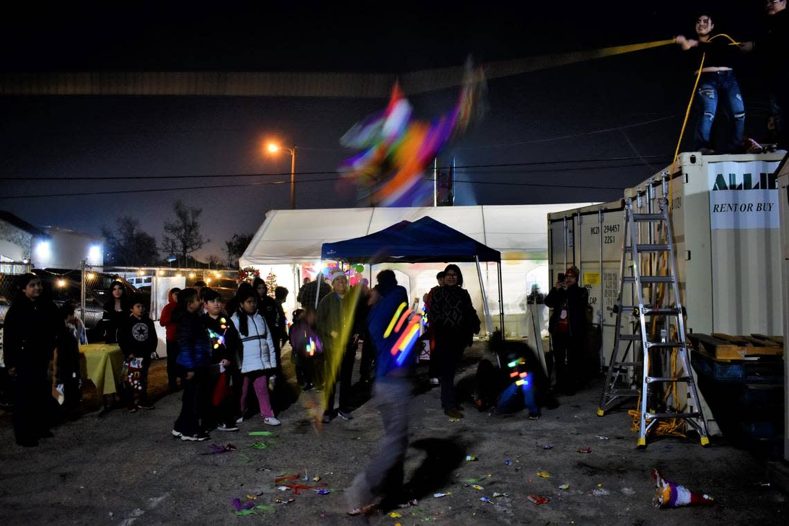A boy swings at a piñata during the Friends of Calwa posada, holiday party, on Friday, Dec. 16, 2022. Other children wait their turn, but a spike of the star piñata has fallen and candy starts to pour on the floor.