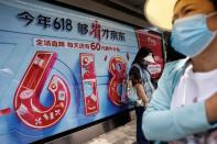 People wait for bus near a billboard of JD.com advertisement for the "618" shopping festival, in Beijing