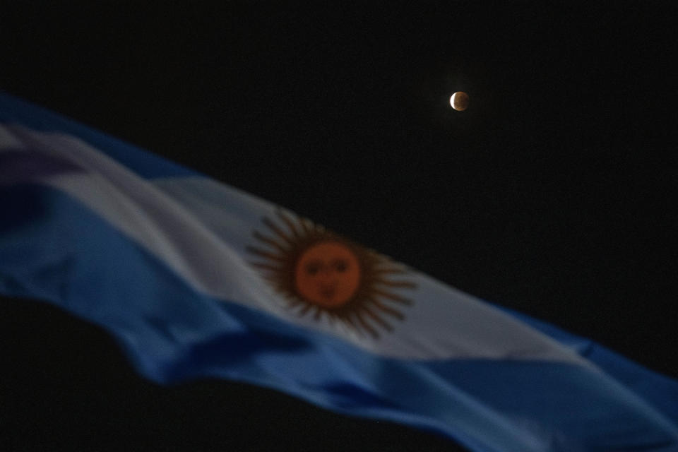 A lunar eclipse is seen behind an Argentinian flag during the first blood moon of the year in Buenos Aires, Argentina, Monday, May 16, 2022. (AP Photo/Rodrigo Abd)