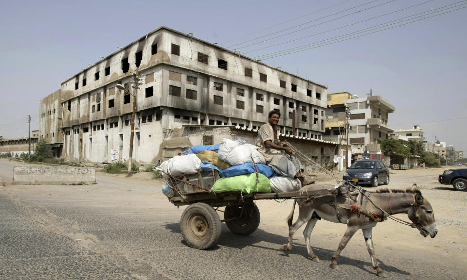 In this Friday, Oct. 19, 2012 photo, a Pakistani man rides a donkey-cart past a garment factory which was burnt last September, in Karachi, Pakistan. At the only morgue in Pakistan's largest city lie the blackened remains of 32 people killed in one of the worst industrial accidents in the country's history, wrapped in white plastic body bags waiting for DNA tests to determine who they are and where they belong. (AP Photo/Fareed Khan)