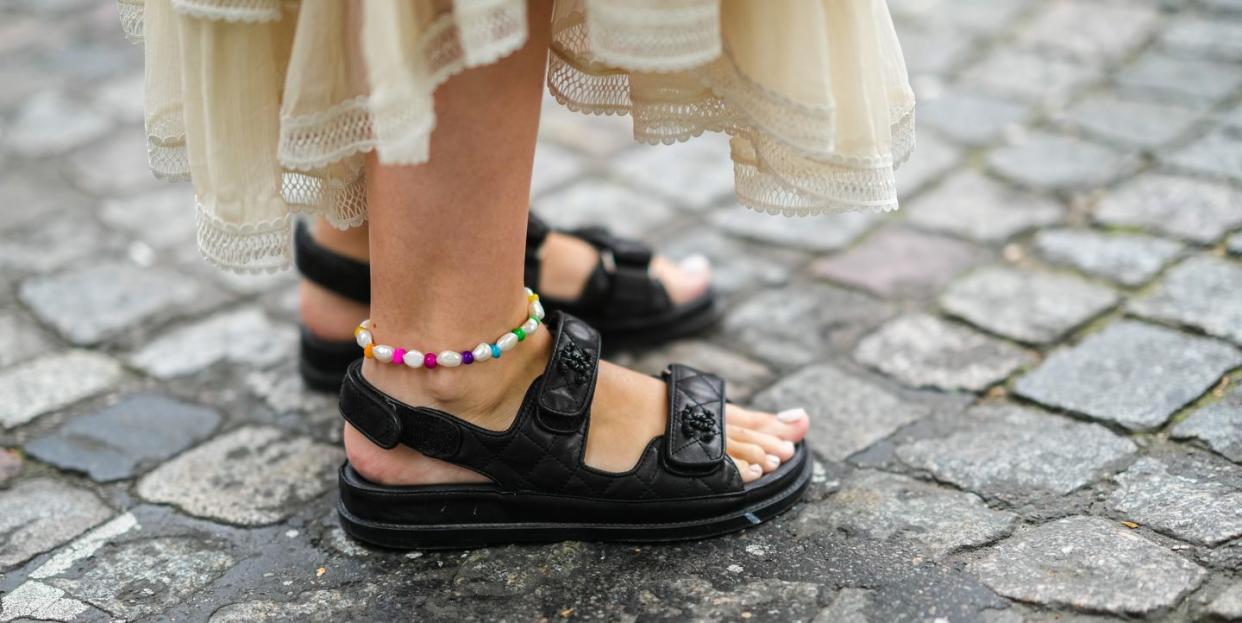 a woman wearing a pearl and colorful bead anklet with black channel sandals and a dress on the street during paris fashion in a roundup of the best anklets for women 2023