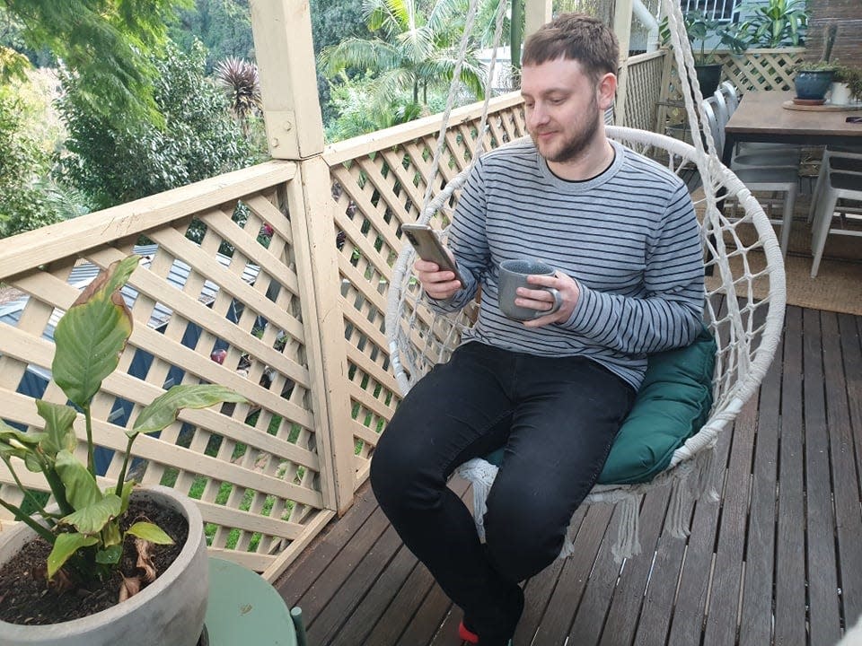 twitch exec lewis mitchell sits on chair swing on porch while drinking coffee and checking phone