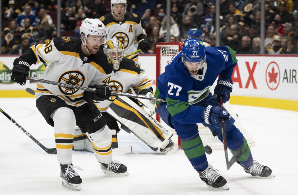 Boston Bruins defenseman Matt Grzelcyk (48) fights for control of the puck with Vancouver Canucks defenseman Travis Hamonic (27) during the second period of an NHL hockey game Wednesday, Dec. 8, 2021 in Vancouver, British, Columbia. (Jonathan Hayward/The Canadian Press via AP)