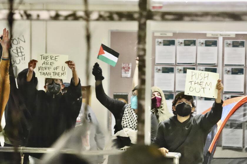Pro-Palestinian protesters hold up signs while occupying a building on the campus of California State Polytechnic University, Humboldt, in Arcata, Calif., Monday, April 22, 2024. Students at the university used furniture, tents, chains and zip ties to block entrances to an academic and administrative building on Monday. University officials closed the campus through Wednesday. (Andrew Goff/Lost Coast Outpost via AP )
