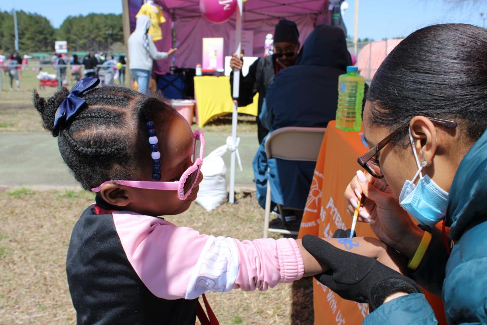 Demarya Thomas with Petersburg Parks & Leisure Services paints a flower on four-year-old Joliana Johnson at Donamatrix Day 2022.