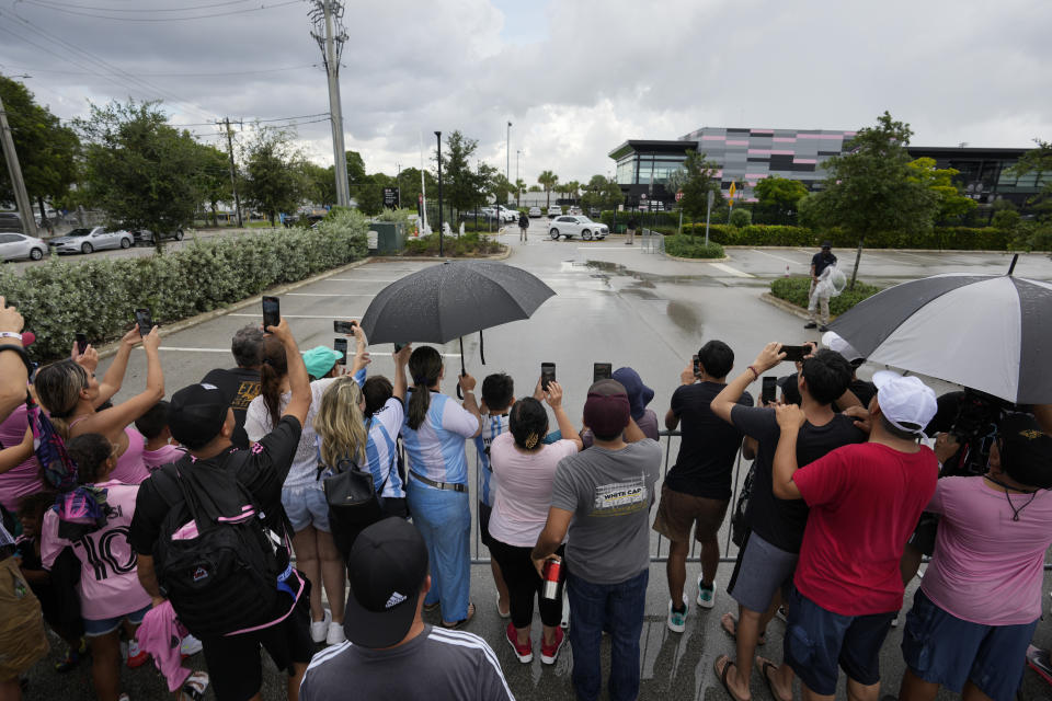 Fans wait in the rain in hopes of catching a glimpse of Lionel Messi, as players' cars leave the Florida Blue Training Center after an Inter Miami MLS soccer team training session, Tuesday, July 18, 2023, in Fort Lauderdale, Fla. (AP Photo/Rebecca Blackwell)