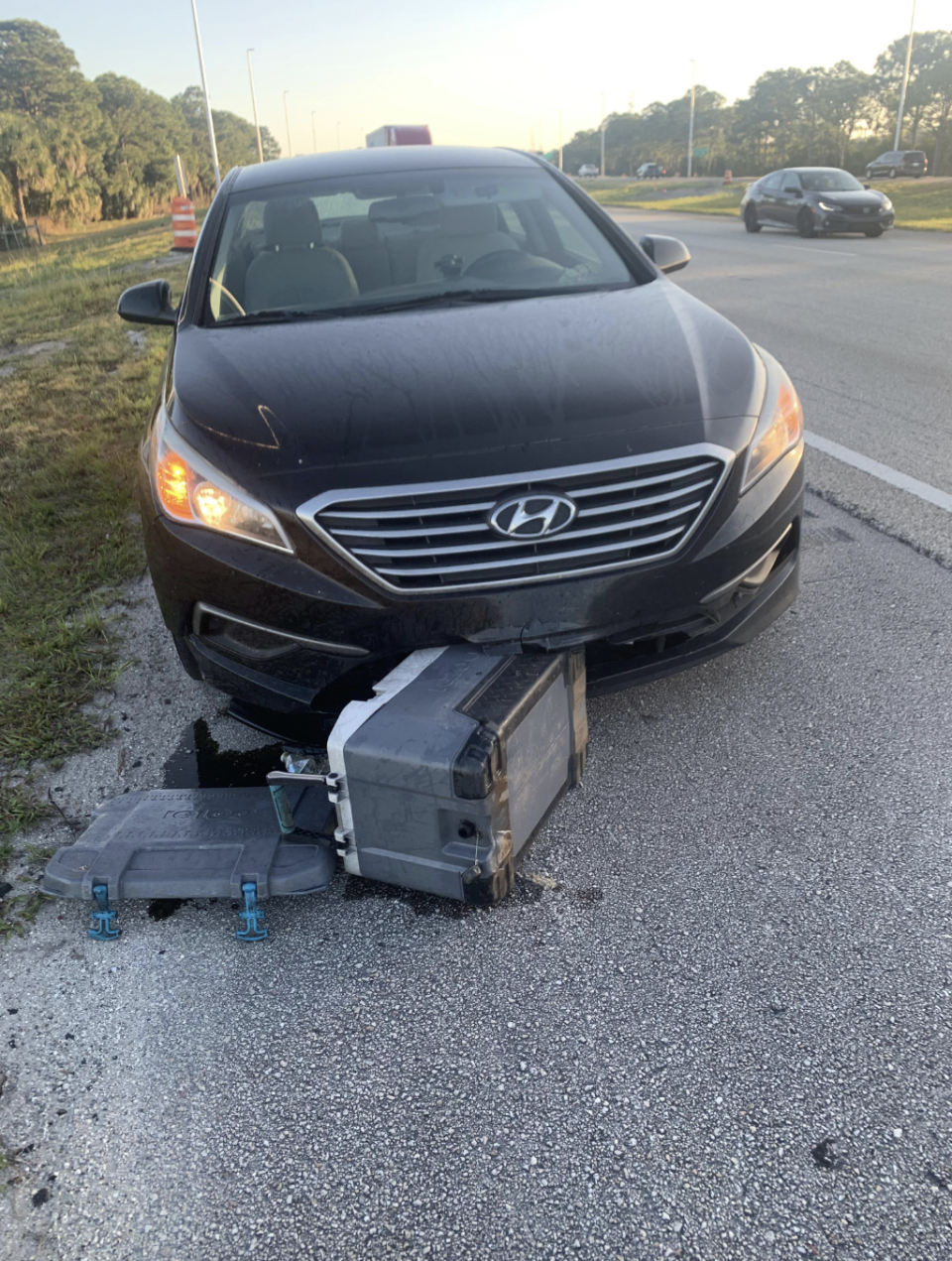 A damaged car with its front bumper fallen off, and debris on the ground beside it