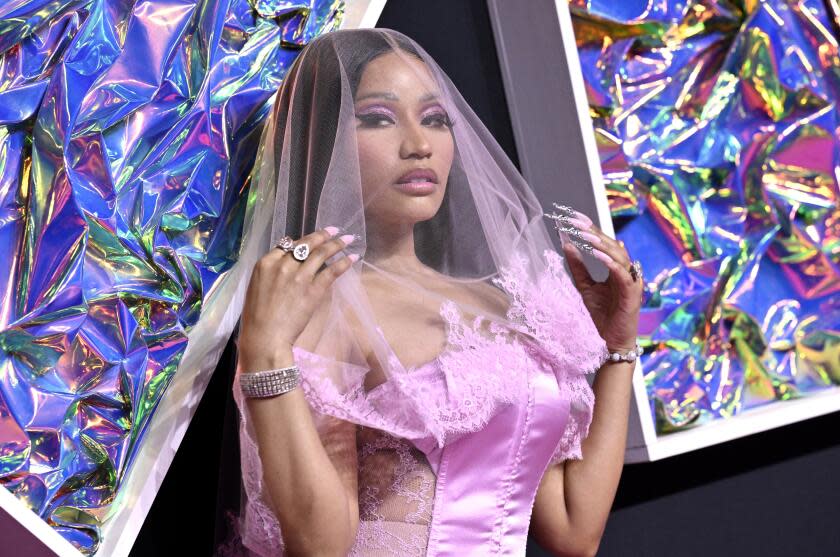 Nicki Minaj in a pink satin corset and a pink veil holding her hands up to her shoulders at a red carpet event