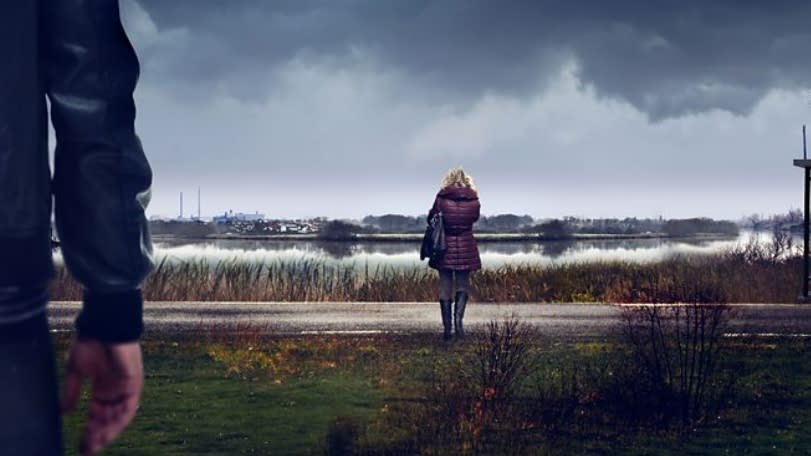  Sambre – Anatomy of a Crime still - woman standing by a river with man watching her from behind . 