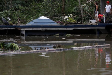 Men stand at the roof of a house submerged by flood waters close to the dam of the Guajataca lake. REUTERS/Carlos Garcia Rawlins